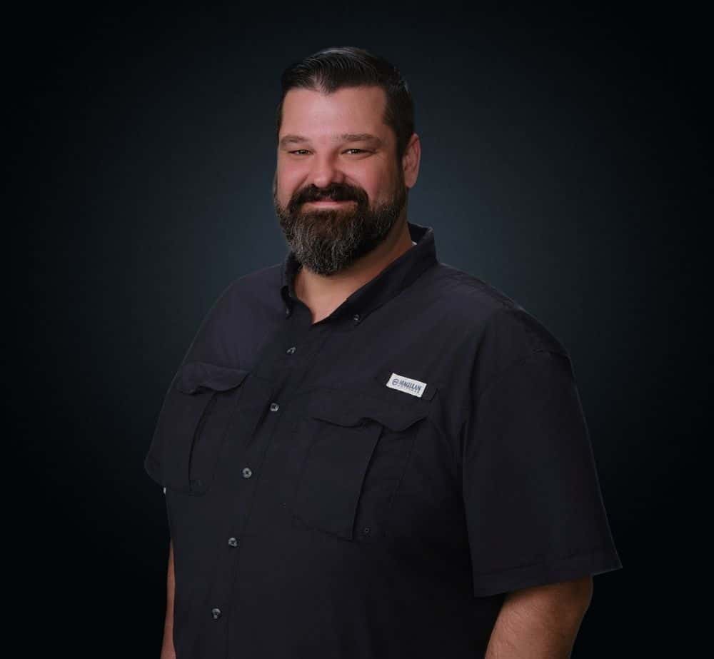Roger Grissom - Live Event Production | Management | Event Producers - Live Event Production | Management | Event Producers Professional portrait of a man with a dark button-up shirt, smiling against a dark studio background.