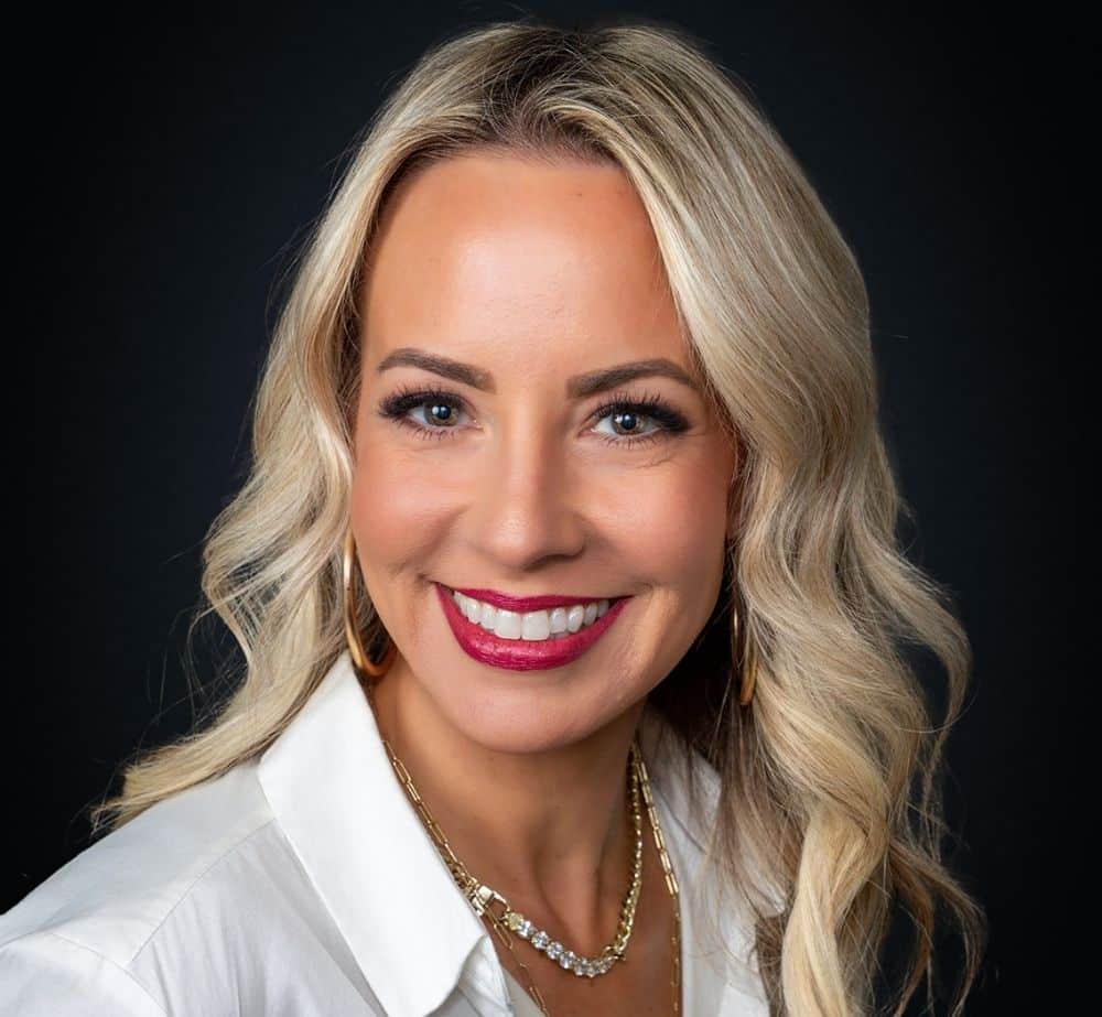 Shana Trosclair - Live Event Production | Management | Event Producers - Live Event Production | Management | Event Producers Portrait of a smiling blonde woman in a white shirt against a dark studio background.