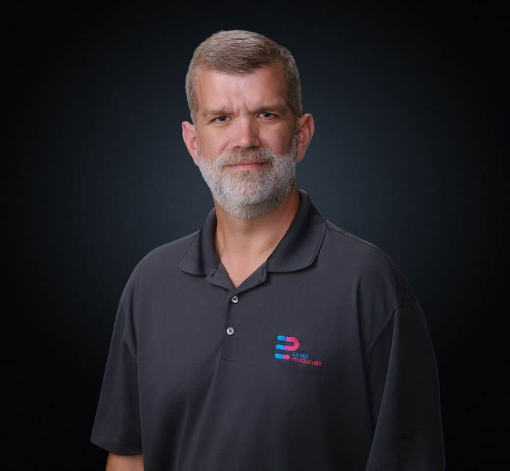 Tyson Grabler - Live Event Production | Management | Event Producers - Live Event Production | Management | Event Producers Portrait of a middle-aged man with a gray beard in a dark polo shirt bearing an Event Producers logo on the chest.